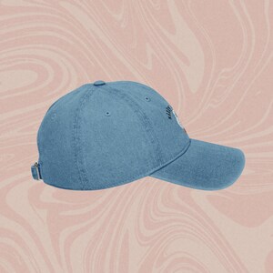May include: A blue denim baseball cap with the text "Silly" embroidered on the front in black.