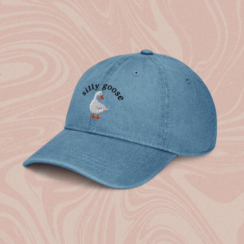 May include: A blue denim baseball cap with the text "silly goose" embroidered in black on the front. A white goose with orange feet is embroidered next to the text.