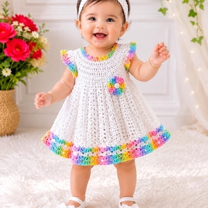May include: A white crochet dress featuring a rainbow-colored trim on the ruffled sleeves and hem, a matching rainbow crochet flower accent on the chest, and a white crochet headband with a bow, paired with white shoes with bow details.