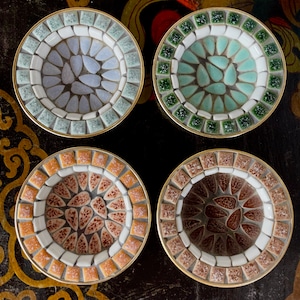 Op de afbeelding: Set van vier mozaïek onderzetters. Elke onderzetter heeft een gouden rand en een uniek patroon. De mozaïektegels zijn in blauw, groen, oranje en bruin. Beschermt oppervlakken tegen kringen van glazen en kopjes.