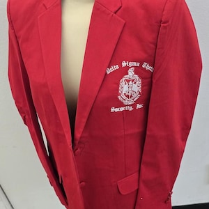 May include: A red blazer with a white embroidered logo that reads "Delta Sigma Theta Sorority, Inc."