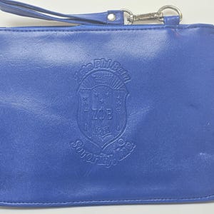 Könnte beinhalten: Eine blaue Leder-Reißverschlusstasche mit einem goldenen, geprägten Wappen, auf dem "Zeta Phi Beta Sorority, Inc. 1920" steht.
