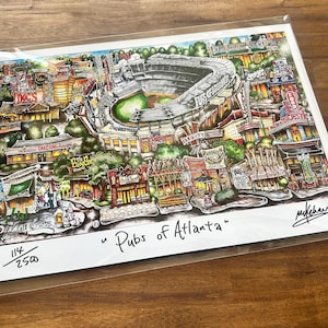 May include: A colorful print titled "Pubs of Atlanta" featuring a detailed illustration of a city scene with a stadium, bars, and restaurants. The artwork is signed and numbered 114/2500.