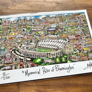 May include: A colorful print titled "Memorial Pubs of Bloomington" featuring a detailed illustration of a stadium and surrounding buildings. The artwork includes various businesses and the score 16-0. The print is numbered 41/2500 and signed by the artist.