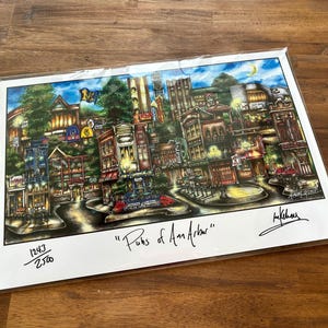 May include: A colorful print titled "Pubs of Ann Arbor" depicting a detailed street scene with buildings, streetlights, and vehicles. The artwork is signed and numbered 1243/2500.