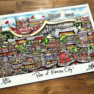 May include: A colorful print titled "Pubs of Kansas City" featuring a detailed illustration of a stadium and various buildings. The artwork includes the text "Pubs of Kansas City" and is numbered 237/2500.