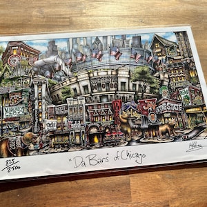 May include: A colorful print titled "Da Bars of Chicago" depicts a detailed illustration of Chicago bars and landmarks. The artwork features buildings, signs, and bears, with the Soldier Field stadium in the background. The print is numbered 825/2500.