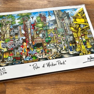 May include: A colorful art print titled Pubs of Wicker Park featuring a detailed urban street scene with numerous storefronts, signs, and architectural elements. The print is numbered 203/2500 and includes a signature in the bottom right corner.