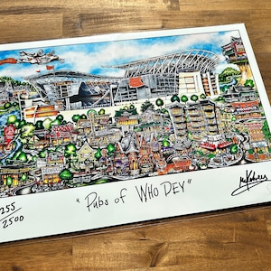 May include: A colorful print titled "Pubs of Who Dey" featuring a detailed illustration of a city with a stadium, buildings, and a plane. The print is numbered 255/2500 and signed by the artist. The artwork is on a white background.