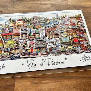 May include: A colorful print titled "Pubs of Durham" featuring a detailed illustration of a street scene with various pub signs and buildings. The artwork is signed and numbered 86/2500.