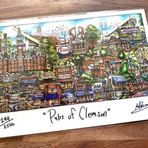 May include: A colorful print titled "Pubs of Clemson" depicts a detailed illustration of a townscape with buildings, signs, and a stadium. The artwork features a variety of colors and architectural styles, with the text "Pubs of Clemson" at the bottom.