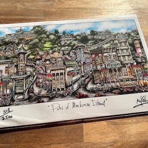 May include: A detailed, colorful print of Mackinac Island pubs, featuring buildings, bicycles, and a horse-drawn carriage. The artwork is signed and numbered, with the title "Pubs of Mackinac Island" visible.