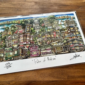 May include: A colorful print titled "Pubs of Madison" featuring a detailed illustration of buildings, shops, and a cityscape. The artwork includes a signature and is numbered 1356/2500. The print is in a protective sleeve.