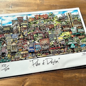 May include: A colorful illustration of a city scene with buildings, streets, and trees. The title "Pubs of Dayton" is written in black at the bottom of the image. The image is numbered 537/1500.