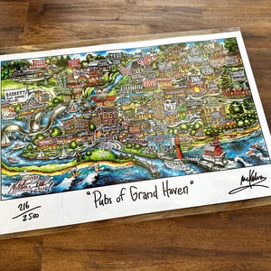 May include: A colorful illustrated map print titled Pubs of Grand Haven featuring various local establishments, a waterfront, and boats. The artwork includes a signature, the text 216/2500, and is enclosed in a clear protective plastic sleeve.