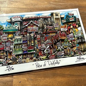 May include: A colorful illustration of a city street scene with buildings and shops. The illustration is titled "Pubs of Dekalb" and includes the text "Home of Northern Illinois University". The illustration is numbered 431/2500.
