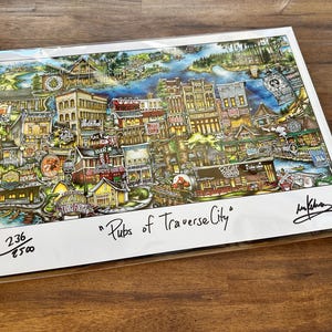 May include: A colorful, detailed art print titled Pubs of Traverse City, featuring a bustling town scene with various buildings, signage, and greenery. The print is numbered 236/500, includes a signature, and is encased in a clear protective sleeve.