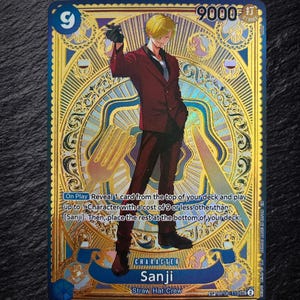 Könnte beinhalten: Eine goldfolierte One Piece Sammelkarte mit der Figur Sanji in einem roten Anzug. Die Karte zeigt eine Stärke von 9000, den Text Sanji, Straw Hat Crew und Spielanweisungen. Der Hintergrund ist mit komplizierten kreisförmigen Mustern und Besteck verziert.