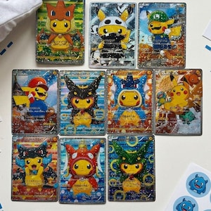 May include: A collection of nine trading cards featuring Pikachu in various costumes. The cards have a holographic effect and are displayed on a white surface. The cards are from the Cardmonster brand.