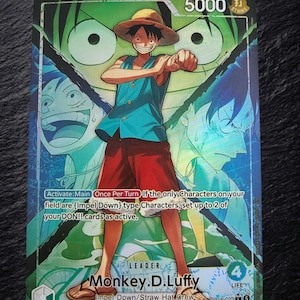 Könnte beinhalten: Eine Sammelkarte mit Monkey D. Luffy, der einen Strohhut, eine blaue Weste und eine rote Hose trägt. Die Karte zeigt eine Stärke von 5000, einen Lebenswert von 4 und Spieltext vor einem Hintergrund in Blau- und Grüntönen.