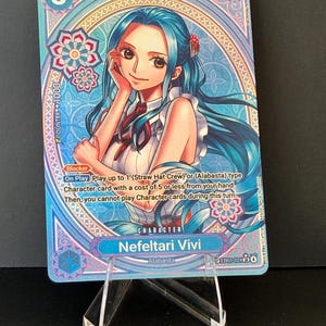 May include: A collectible trading card featuring the character Nefeltari Vivi from the anime series. The card has a blue and white design with a portrait of the character, the number 5, and the text "4000".