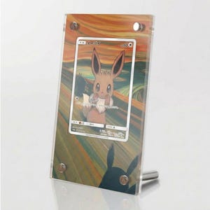 Könnte beinhalten: Ein transparenter Acryl-Displayrahmen mit einer japanischen Eevee-Sammelkarte. Die Karte zeigt ein braunes Eevee-Wesen mit überraschtem Gesichtsausdruck vor einem Hintergrund mit wirbelnden orangefarbenen und grünen Linien. Vier silberne Metallschrauben halten den Rahmen zusammen.