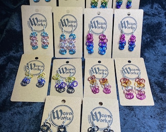 May include: A collection of colorful chainmail earrings displayed on tan cards. The earrings feature various color combinations, including rainbow, pink, blue, and purple. Each card has the "Weave Works" logo.
