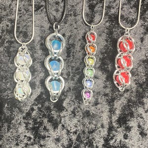 May include: Five silver chain necklaces with different colored glass bead pendants. The pendants are made of multiple beads in a row. The beads are iridescent, blue, rainbow, and red.