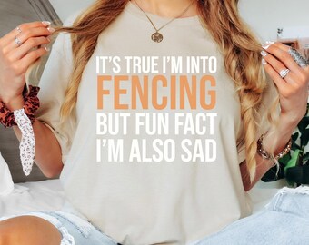 May include: A white t-shirt with the text "It's true I'm into fencing but fun fact I'm also sad" printed in orange.
