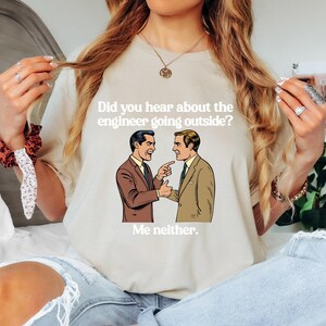 May include: A beige t-shirt with the text "Did you hear about the engineer going outside? Me neither." and a cartoon image of two men in suits.
