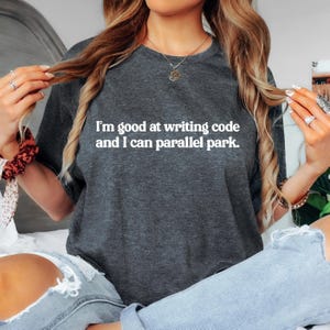 May include: A dark grey t-shirt with the text "I'm good at writing code and I can parallel park." printed in white.
