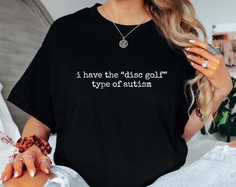 May include: Black t-shirt with the text "i have the "disc golf" type of autism" in white. The shirt is a casual style, suitable for everyday wear. The text is centered on the front of the shirt.