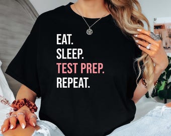 Könnte beinhalten: Schwarzes T-Shirt mit weißem Text, der "Essen. Schlafen. Testvorbereitung. Wiederholen." lautet. Der Text "Testvorbereitung" ist in Pink.
