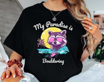 Può includere: Maglietta nera con una grafica di un procione con occhiali da sole e una palma. Il testo "My Paradise is Bouldering" è stampato sulla maglietta.
