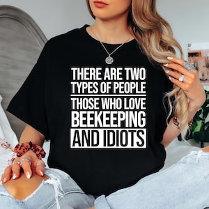 May include: Black t-shirt with white text that reads: "THERE ARE TWO TYPES OF PEOPLE THOSE WHO LOVE BEEKEEPING AND IDIOTS." The shirt is a crew neck and appears to be made of a soft material.
