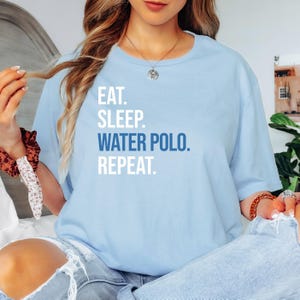 May include: A light blue t-shirt with the text "Eat. Sleep. Water Polo. Repeat." in white and blue lettering.