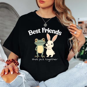 May include: Black t-shirt with a green frog and white rabbit holding hands. The text "Best Friends shot put together" is printed on the shirt.