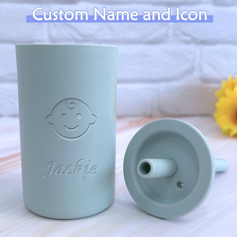 May include: A light blue silicone cup with a baby icon and the name "Jackie" printed on it. The cup has a matching light blue silicone lid with a straw.