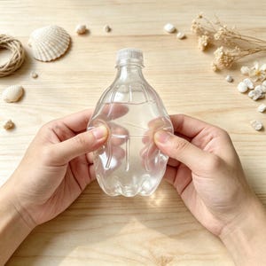 Könnte beinhalten: Eine durchsichtige, leere Kunststoffflasche mit einem bauchigen Körper und einem gerippten Schraubverschluss. Die Flasche weist vertikale Einkerbungen an den Seiten auf, die für eine strukturierte, facettierte Optik sorgen. Das Material ist glatt.