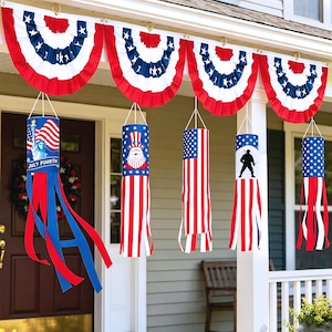 May include: Four pleated red, white, and blue bunting fans hang above five cylindrical wind socks. The wind socks feature patriotic designs including the Statue of Liberty with the text JULY FOURTH, a bearded figure in a top hat, and stars and stripes.