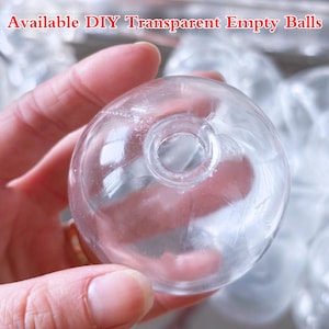 May include: A clear, transparent, empty ball with a hole at the top. The text "Available DIY Transparent Empty Balls" is visible at the top of the image. The ball is held in a hand, with other similar balls visible in the background.