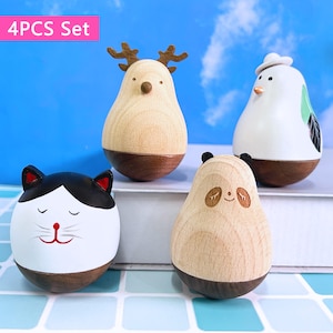 May include: Four wooden animal figurines: a cat, a deer, a panda, and a bird. The cat is white with black and red details. The deer has antlers. The panda has black ears. The bird wears a white hat. The text "4PCS Set" is visible. Each figurine has a dark brown base.