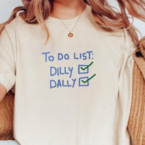 Könnte beinhalten: Ein weißes T-Shirt mit dem Text "To do list: Dilly Dally" in blau geschrieben, mit Kontrollkästchen und grünen Häkchen.