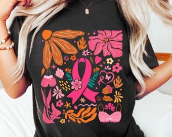 May include: A black t-shirt with a pink ribbon, flowers, and other symbols in a square design. The design is in shades of pink, orange, and brown.