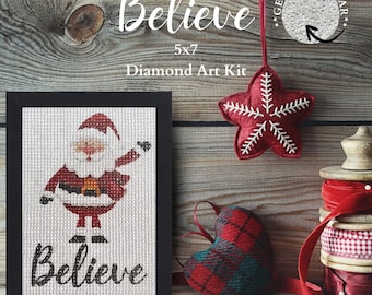 May include: A framed 5x7 inch diamond art kit featuring a Santa Claus design, with the word "Believe" in cursive. A red star-shaped ornament and a plaid heart-shaped ornament are also visible, along with spools of red ribbon.
