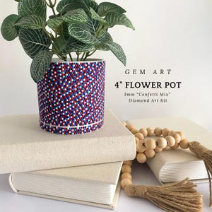 May include: A 4-inch flower pot decorated with red, white, and blue gems, resembling a confetti mix. The pot holds a green plant with white-veined leaves. The text "GEM ART" and "Diamond Art Kit" are visible.
