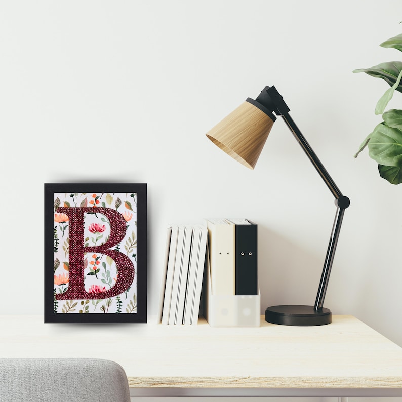 May include: A framed print of the letter "B" with a floral design. The letter is made of burgundy fabric and the flowers are in shades of pink, orange, and green. The frame is black.