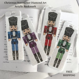 May include: Four white bookmarks with a diamond art design of a Nutcracker. Each bookmark features a different color Nutcracker: blue, purple, red, and green. The bookmarks have a tassel at the top.