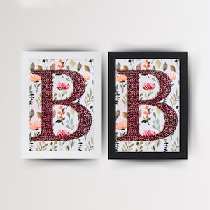 May include: Two framed pictures of the letter "B" made of red sequins on a white background with a floral pattern. The frames are white and black.