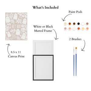 May include: A Halloween-themed art kit includes an 8.5 x 11 inch canvas print with ghosts and the text "HEY BOO", paint pods, two brushes, and a white or black matted frame. The kit provides all the necessary materials for creating artwork.